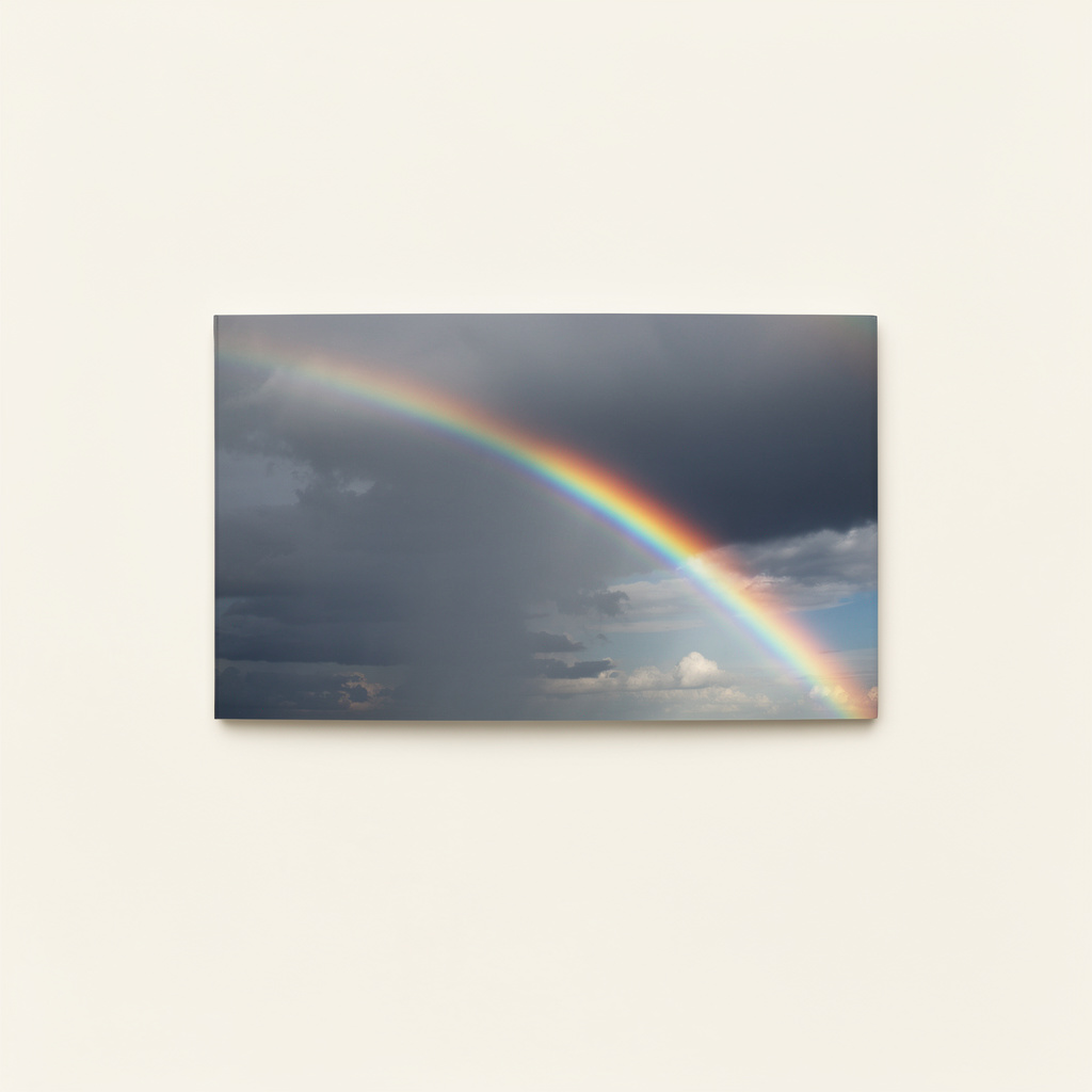 A vivid rainbow arcs diagonally across dark, stormy clouds and patches of pale sky.