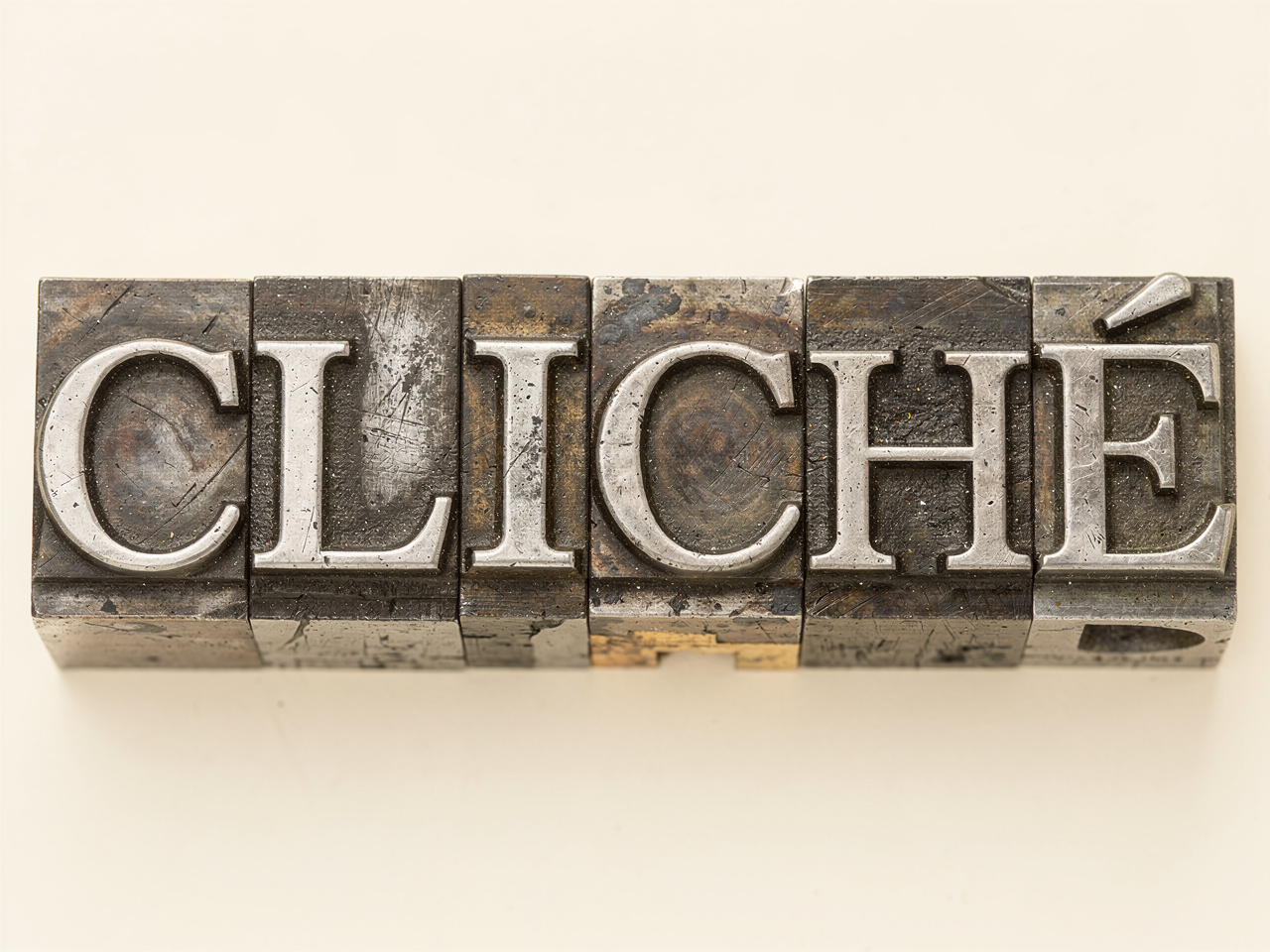 Metal letterpress type blocks arranged horizontally to spell out the word "CLICHÉ" in capital serif letters.