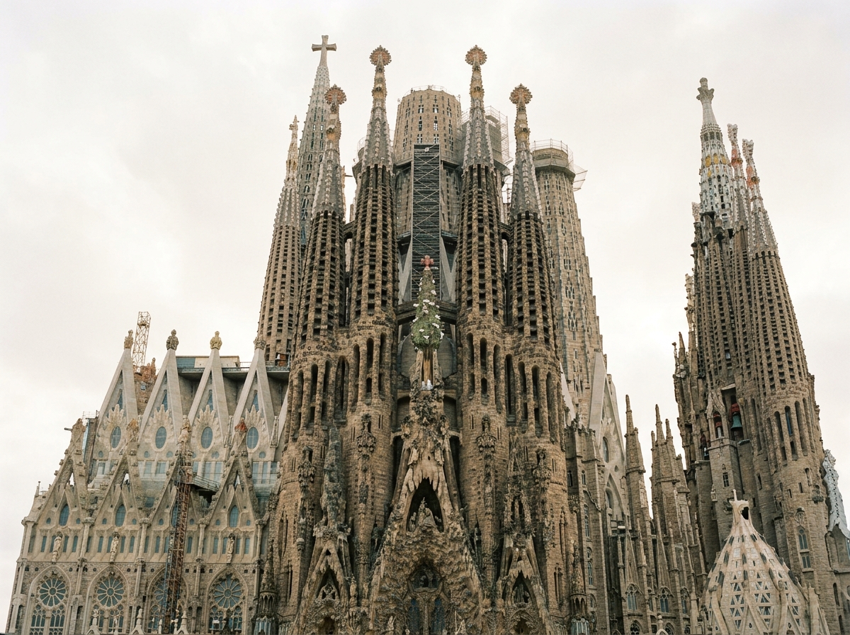 The Sagrada Família in Barcelona features intricate stone spires and sculpted facades rising against an overcast sky.