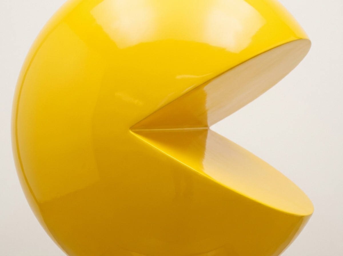 A glossy yellow Pac-Man sculpture shown in profile with its wide triangular mouth open.