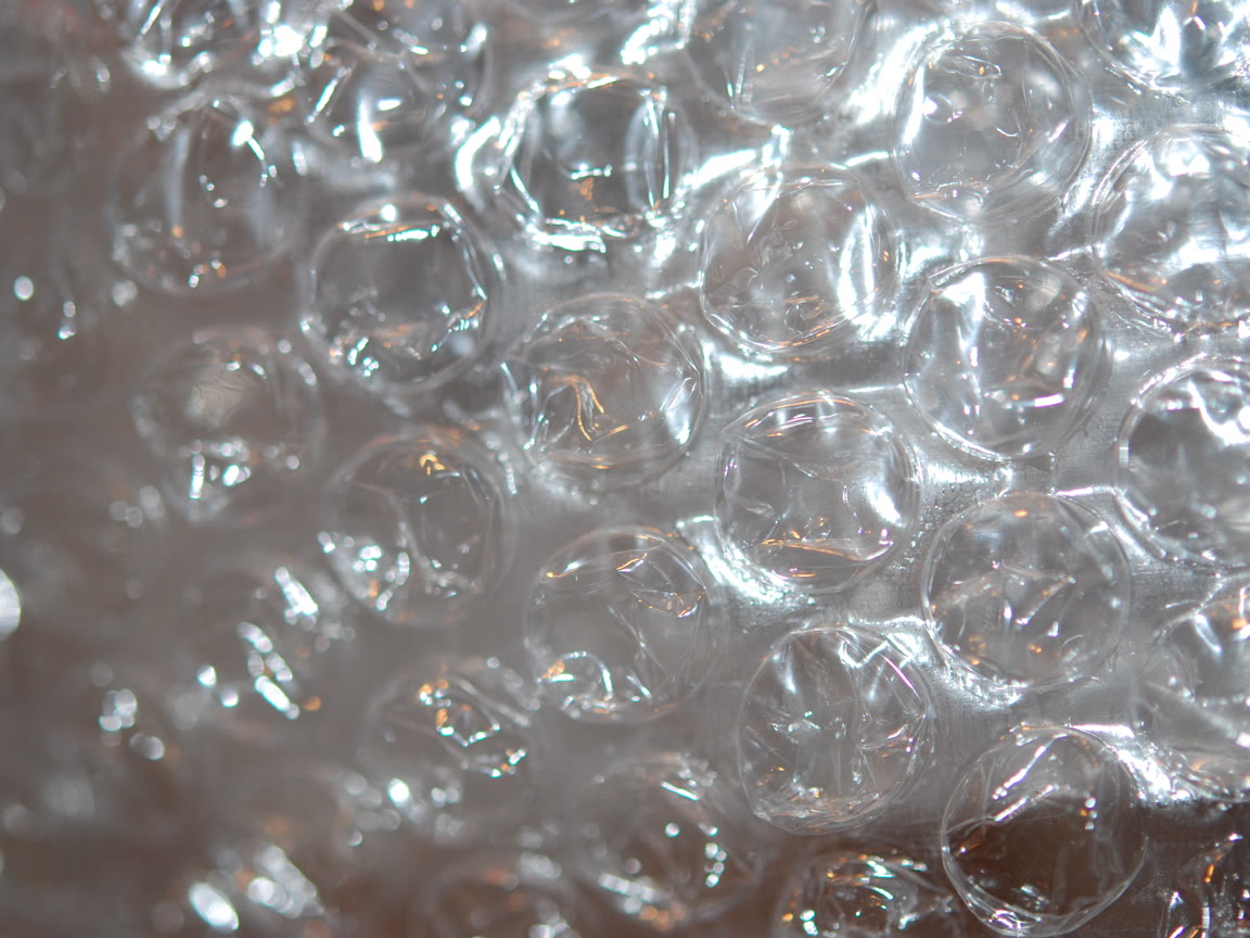 A close-up view of transparent plastic bubble wrap with light reflecting off its circular air bubbles.