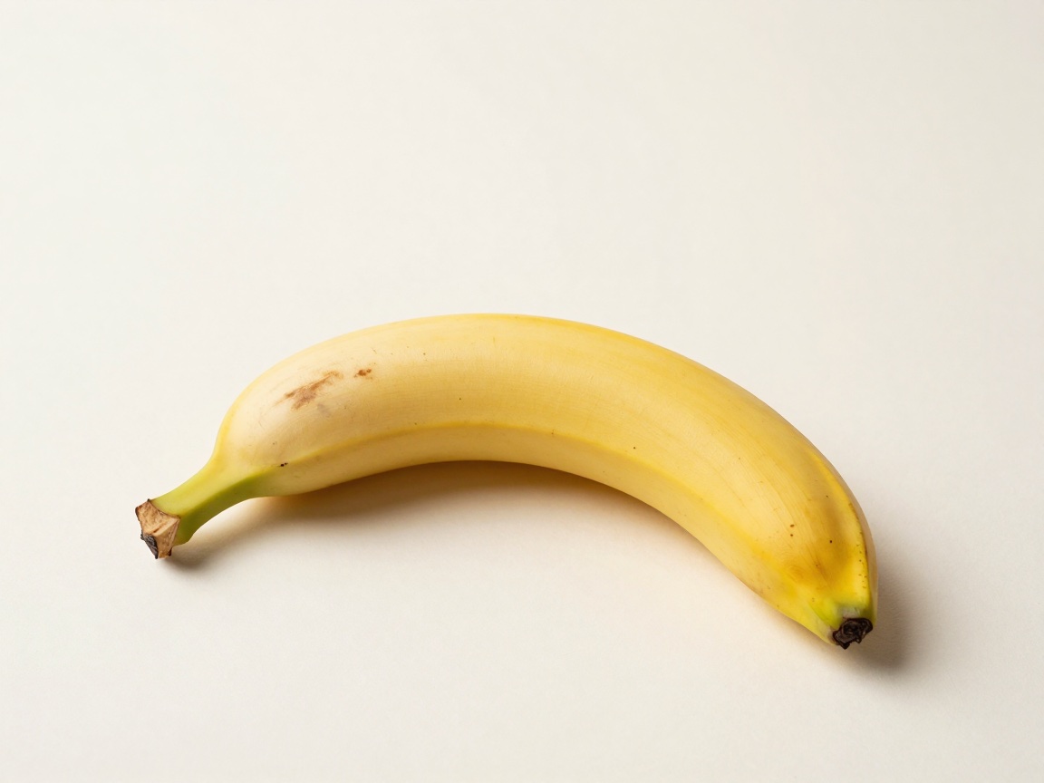 A single ripe yellow banana lies on its side with a few brown freckles on the peel and its stem pointing left.